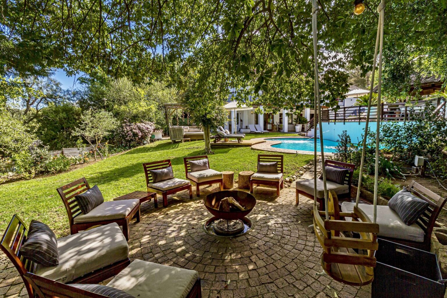 The garden lounge with seating around a fire pit, and the pool behind it